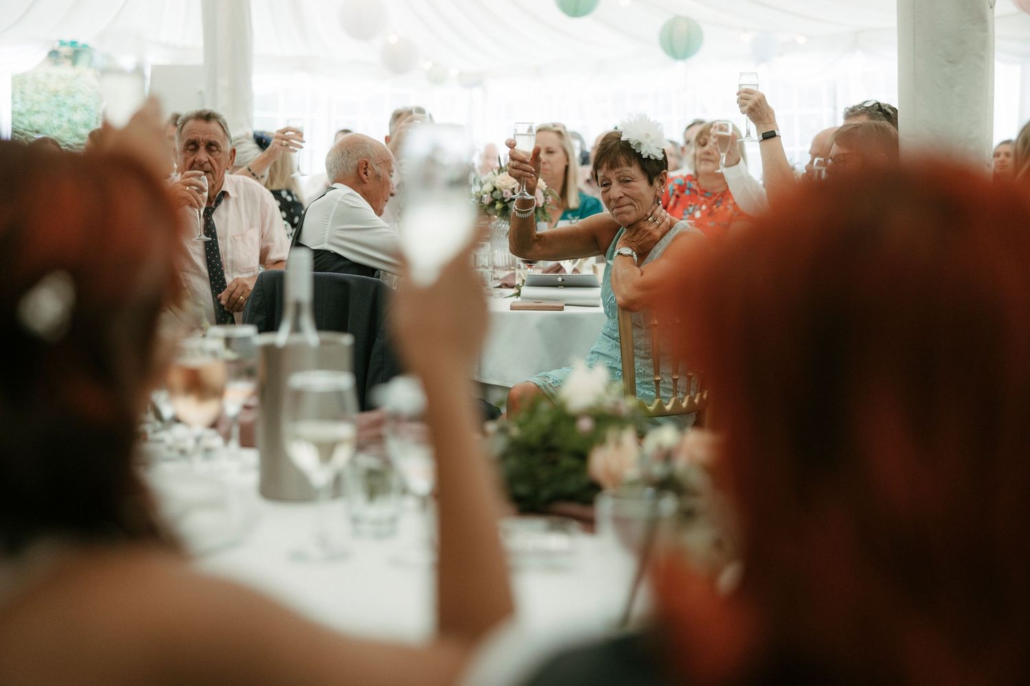 Guests raising glasses in a toast at an elegant wedding reception inside a decorated marquee tent.