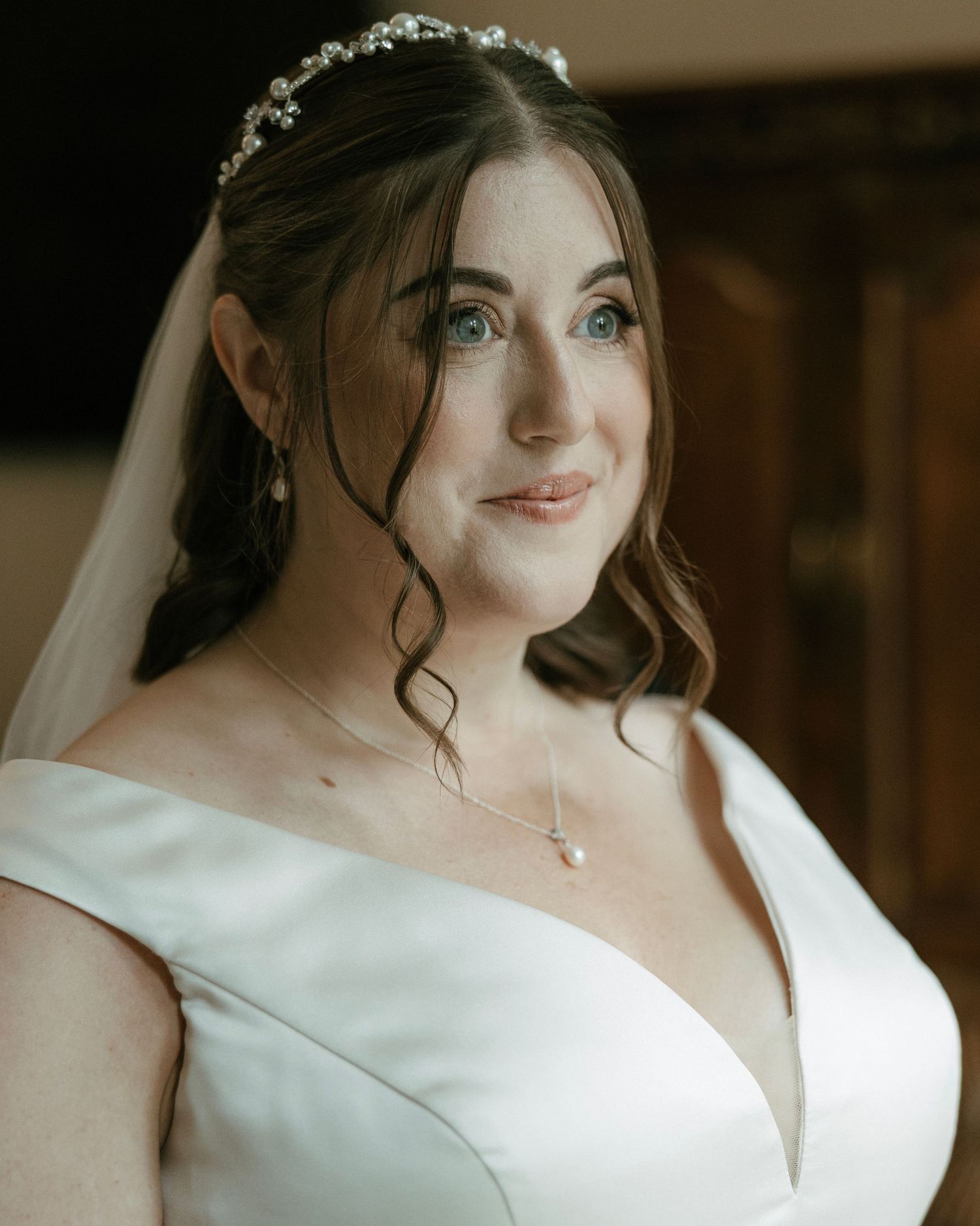 Close-up portrait of a bride wearing a crystal tiara, veil, and pearl necklace with striking blue eyes.