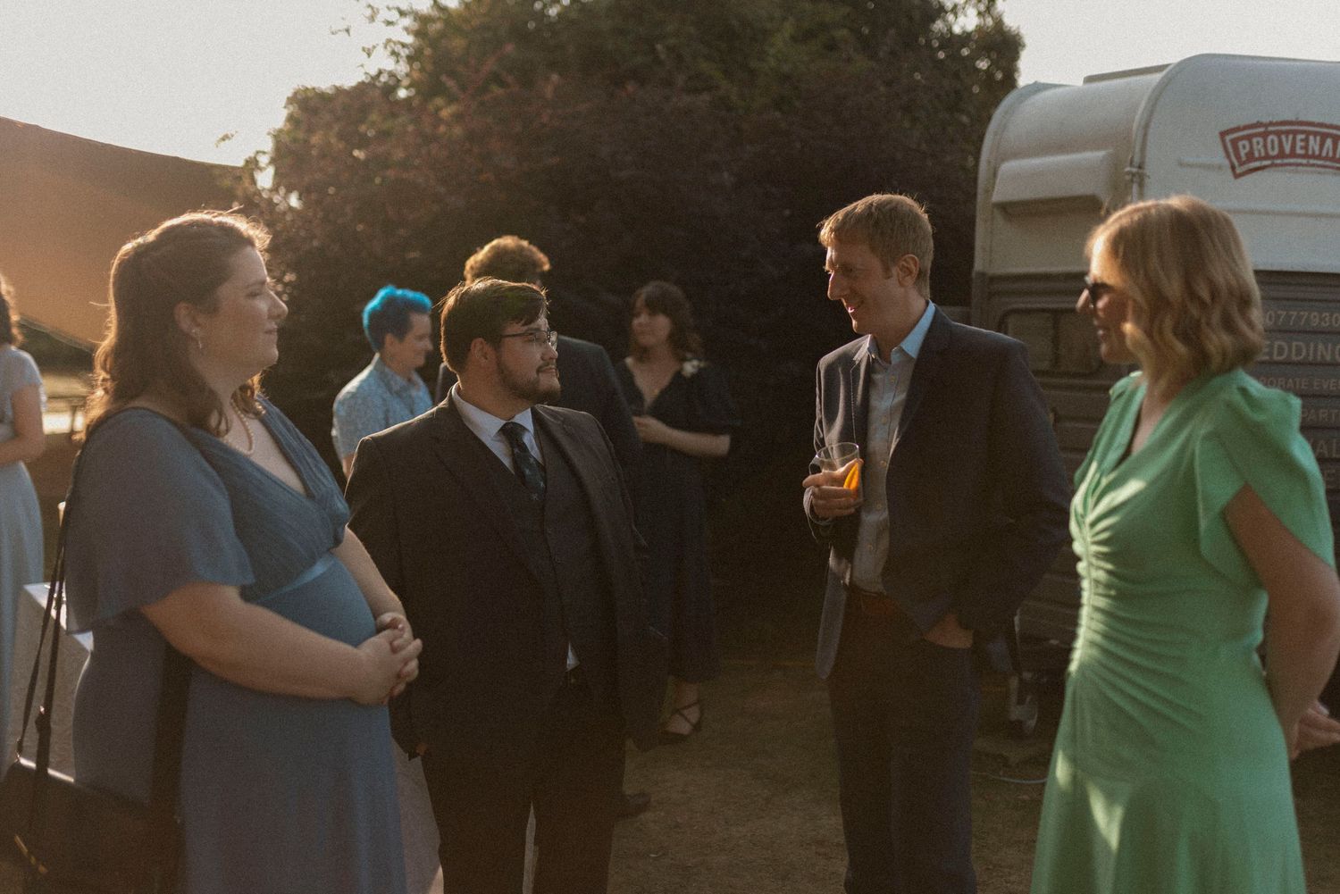 Elegantly dressed guests socializing outdoors at a garden wedding reception during golden hour.