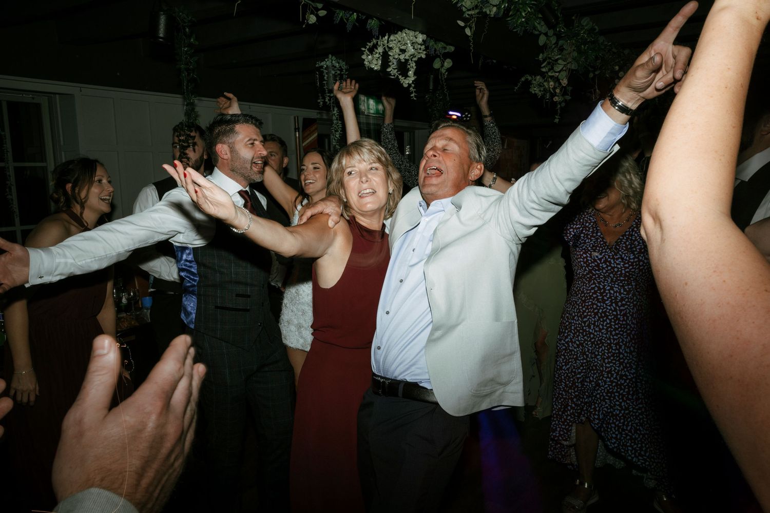 Energetic partygoers dance with their arms raised on a dark dance floor at a lively celebration event.