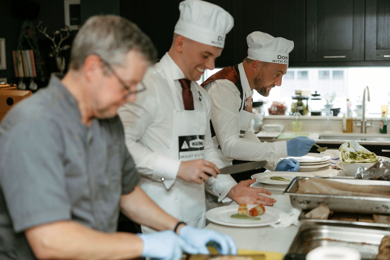 Professional kitchen staff wearing white chef coats and gloves prepare food at a commercial prep station.