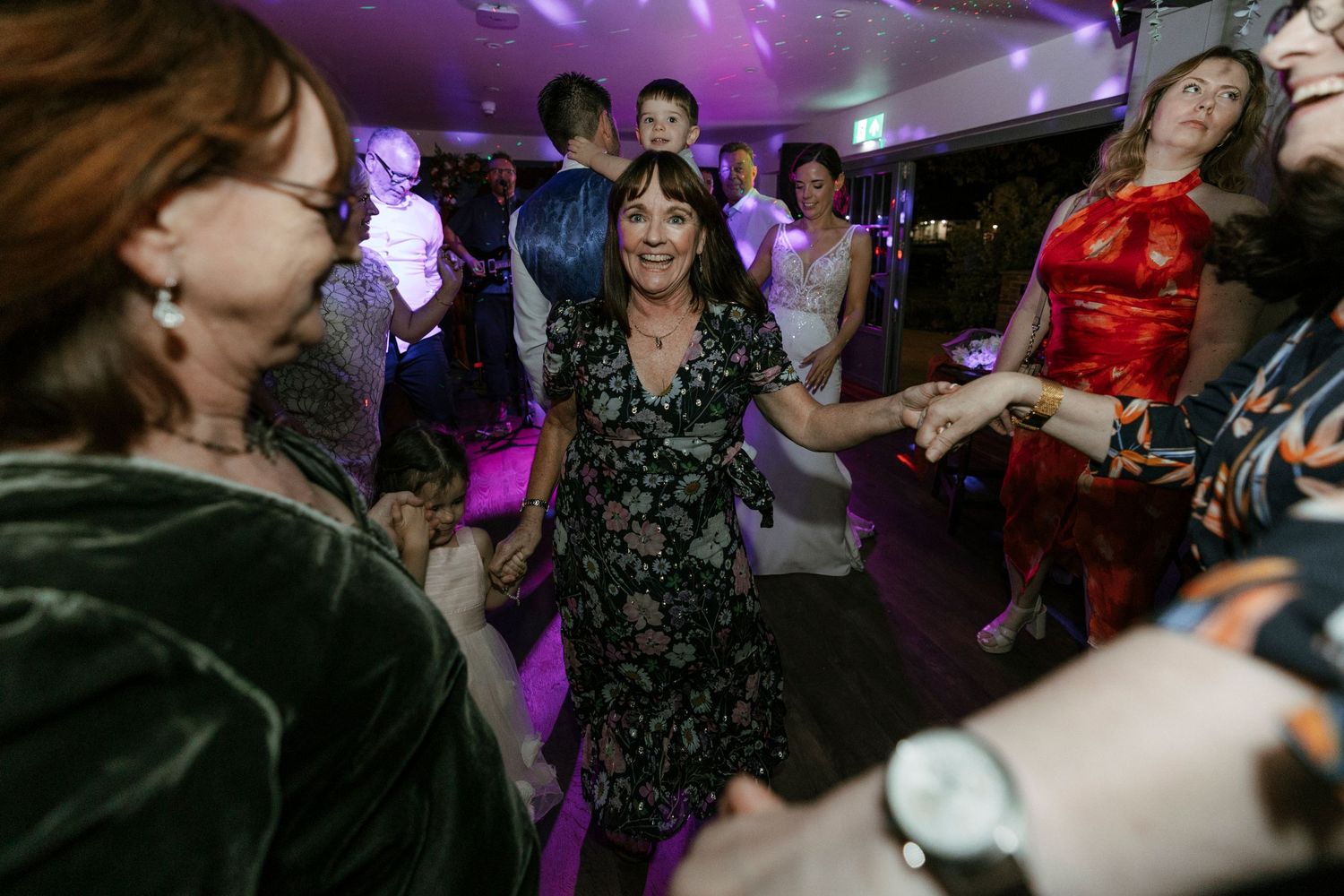 Wedding reception dance party with guests dancing under purple lighting.