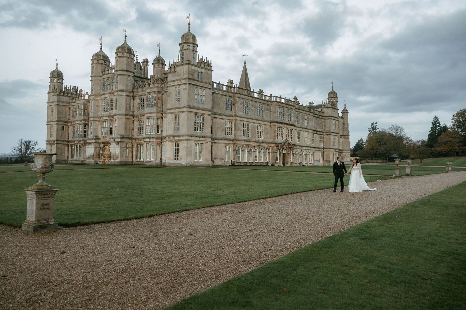 A panoramic view of Burghley House, a grand Elizabethan estate in England, under dramatic cloudy skies.
