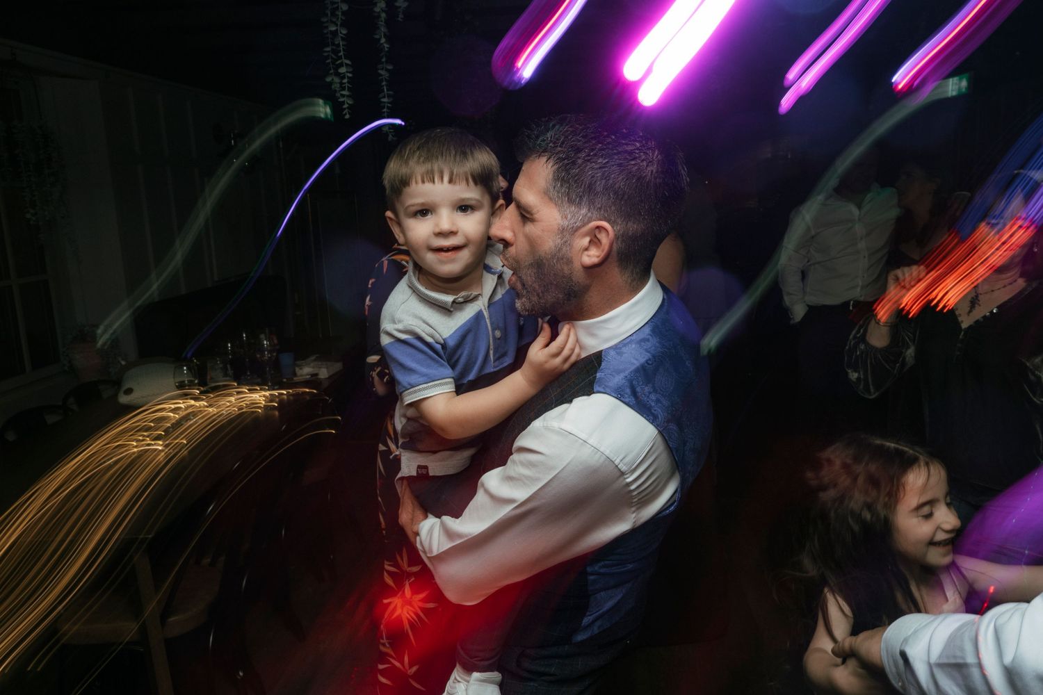 People dancing at a party with colorful neon lighting and glowing effects in a dark room.