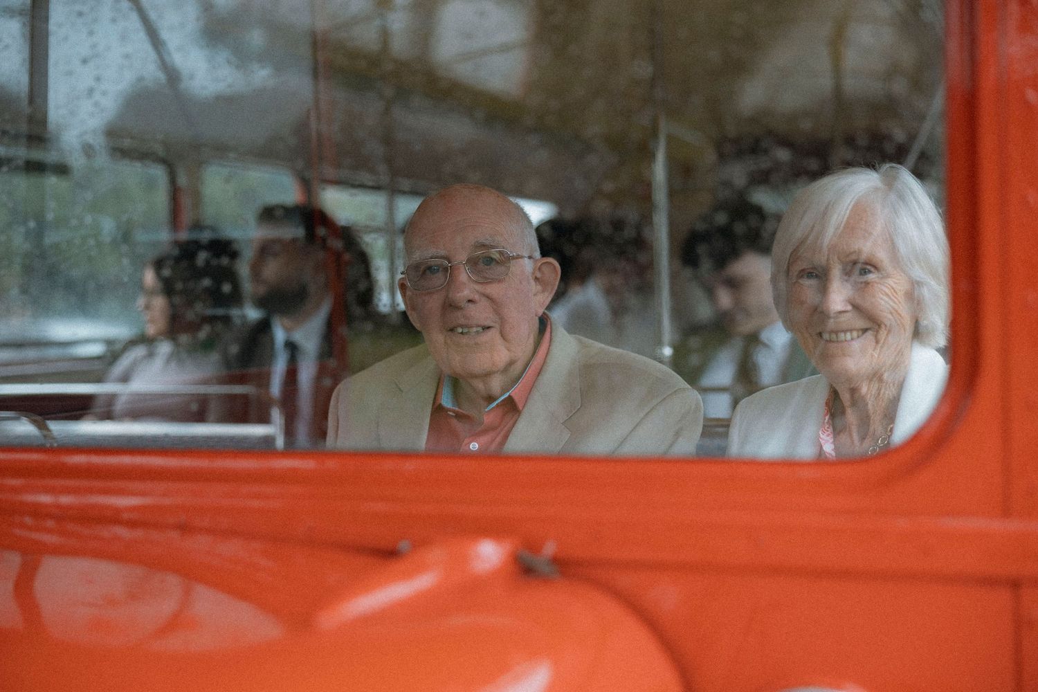 Elderly couple smiling inside a vintage red vehicle, enjoying a scenic ride together.