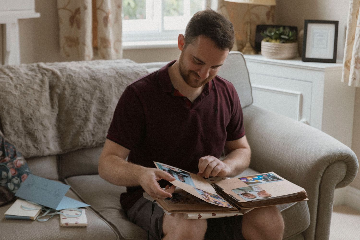 Man sitting on sofa looking through a photo album in a cozy living room.