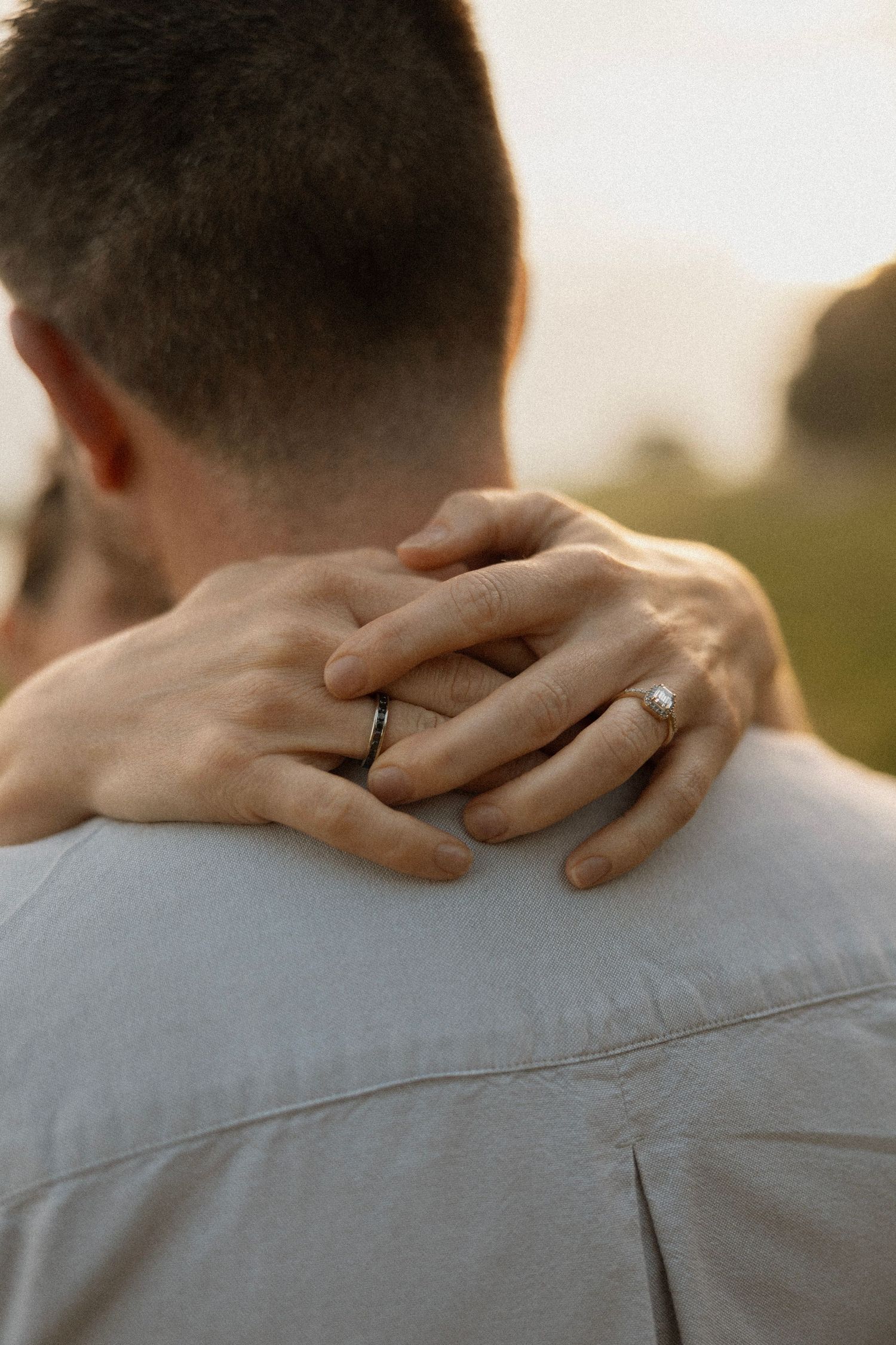 Close-up of hands with wedding rings embracing against white shirt.
