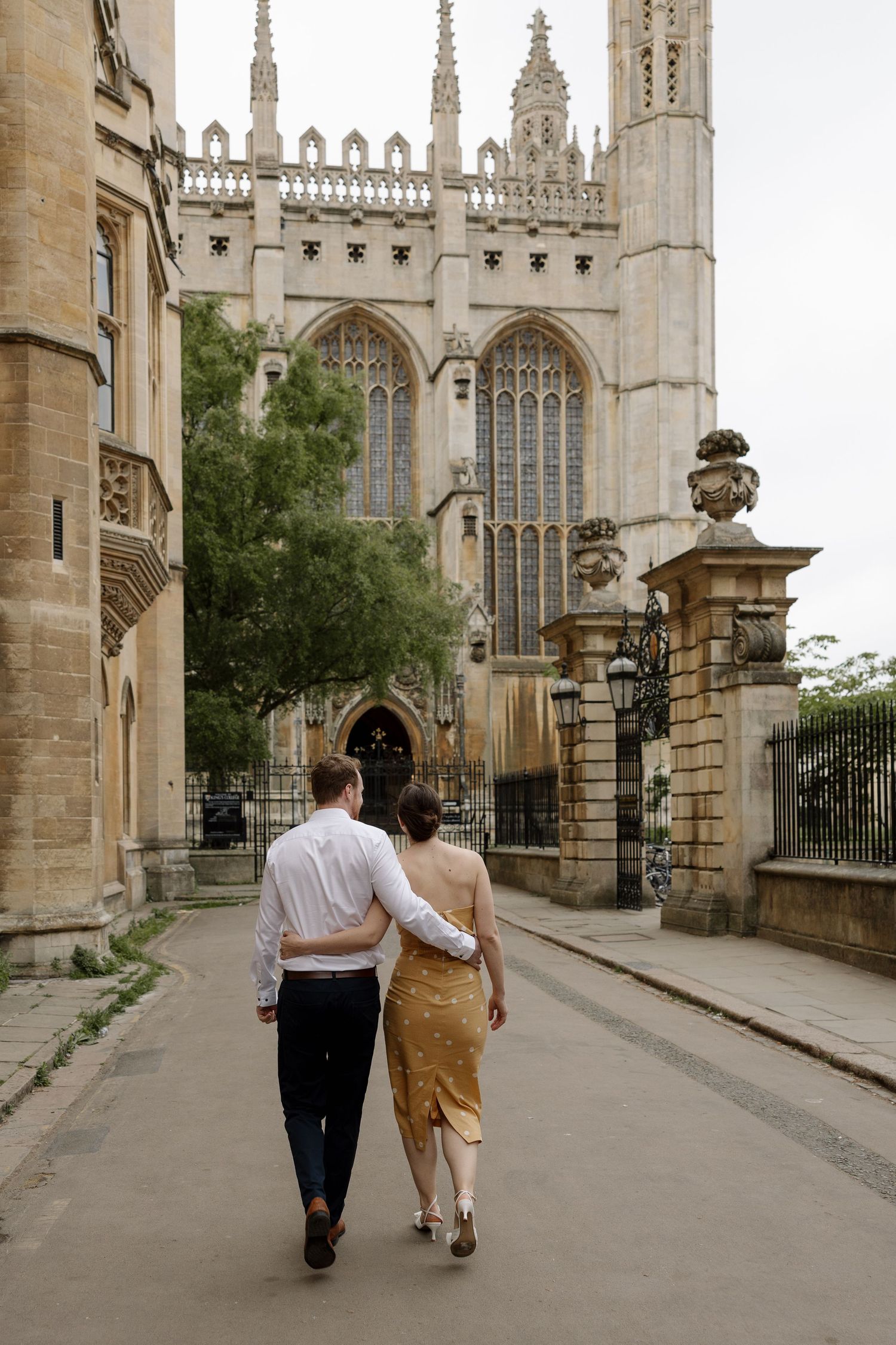 Couple walking arm in arm toward a grand Gothic cathedral on a cobblestone path in a historic European city.