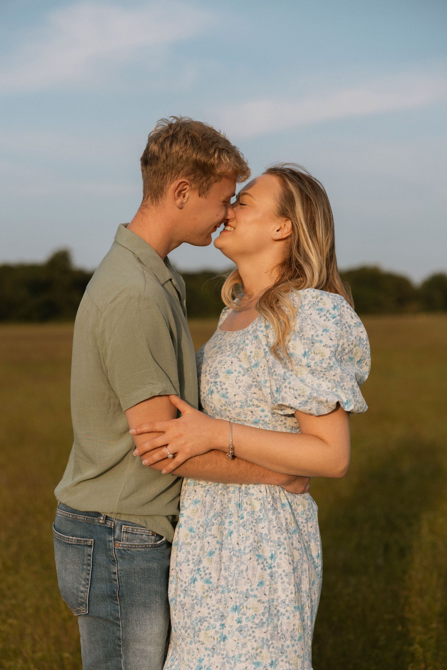A couple shares a romantic almost-kiss while embracing in a sunlit green field.