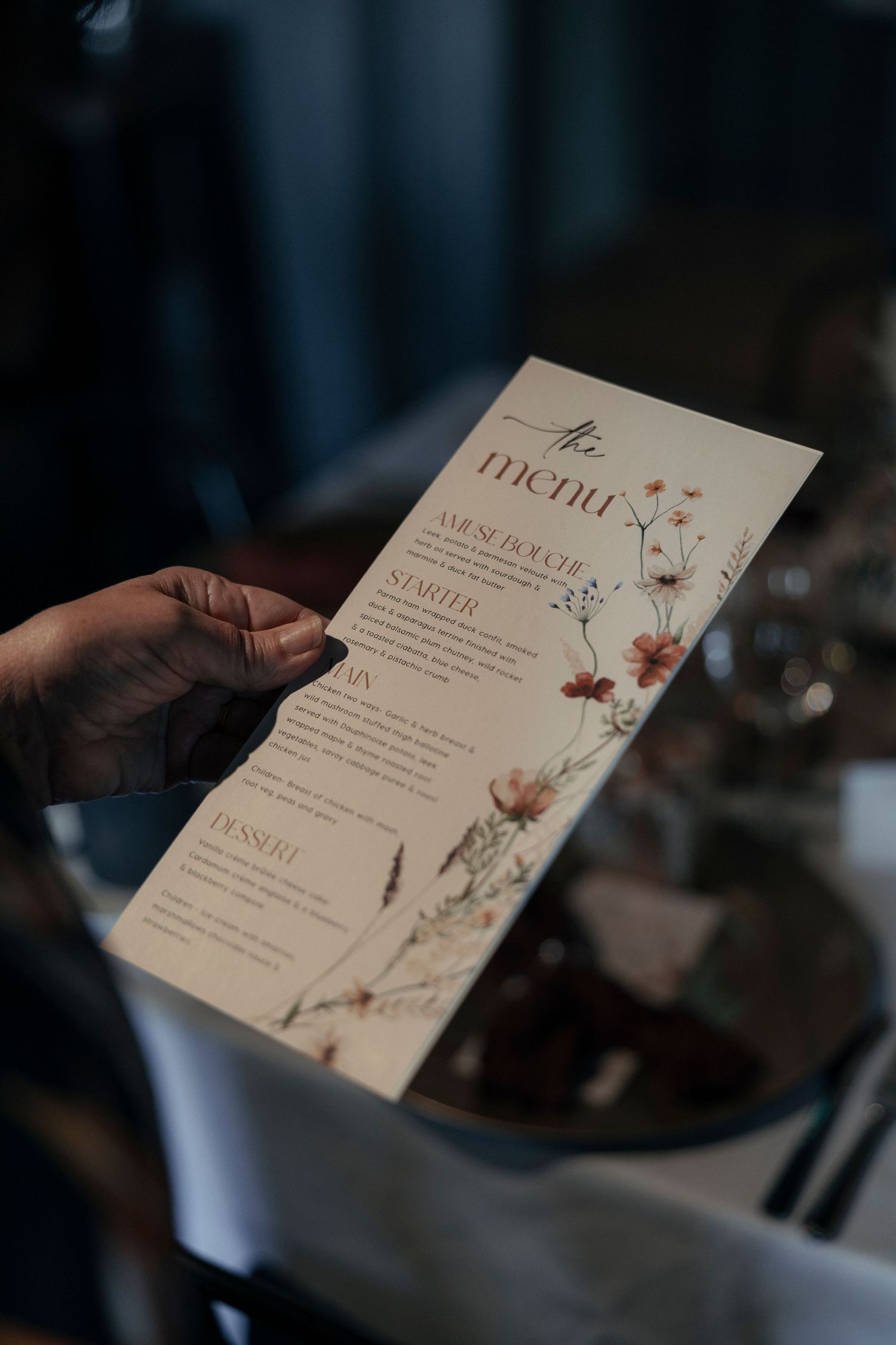 Hand holding an elegant floral wedding menu card with sections for starter, main, and dessert courses.