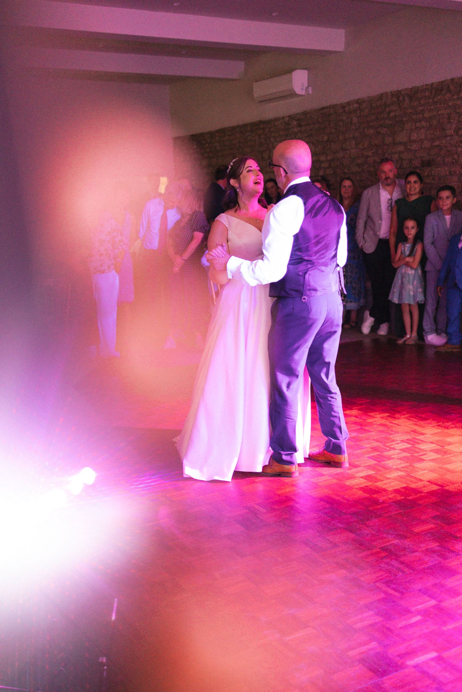 Bride and groom sharing their first dance under pink and purple wedding reception lighting.
