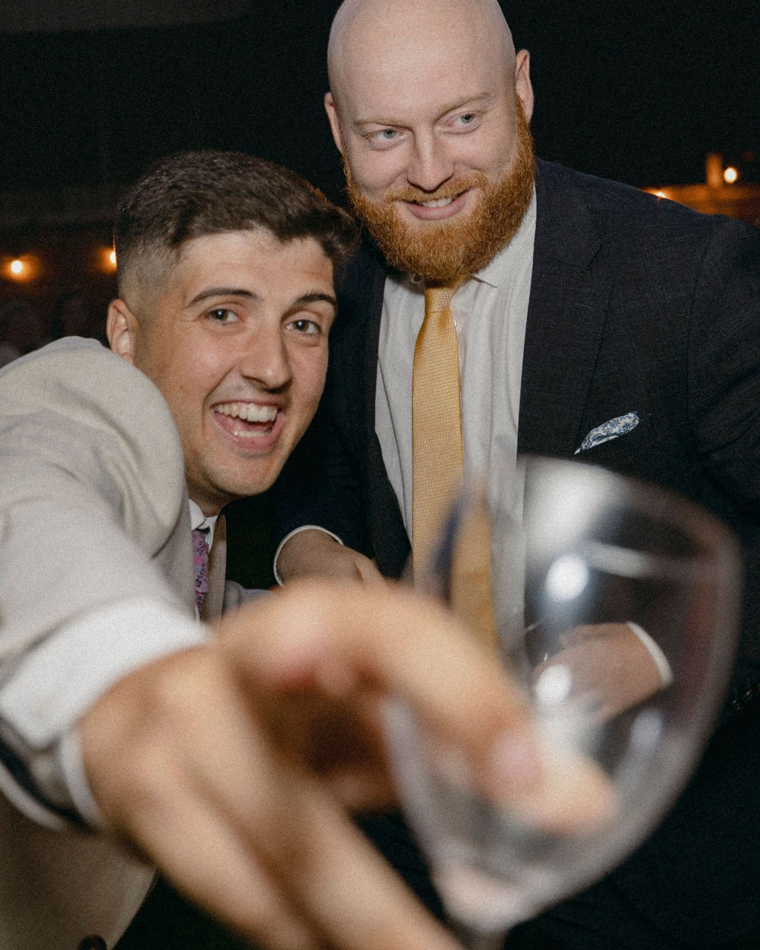 Two men in suits smiling and toasting with a wine glass at a formal event.