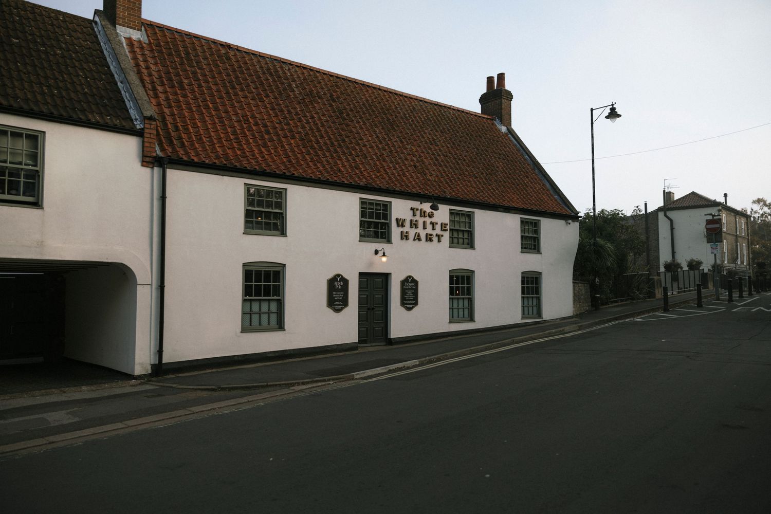 The White Hart pub, a whitewashed building with red-tiled roof on a quiet street corner in an English village.