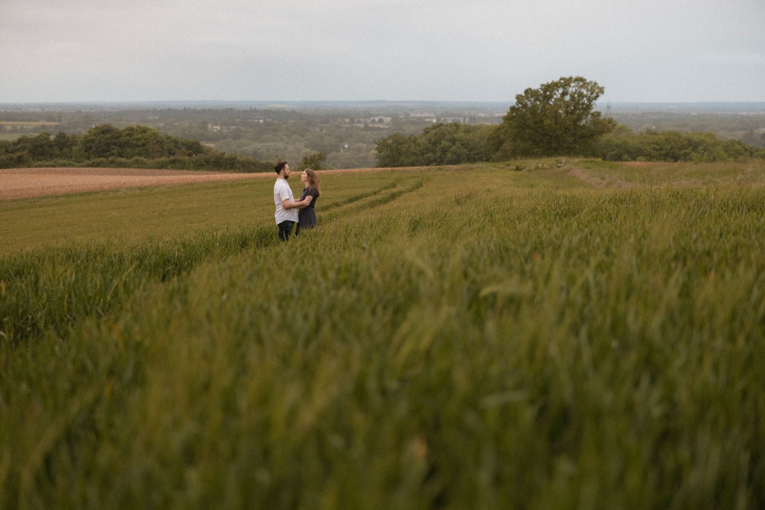 Two figures walking together through a scenic hilltop meadow with expansive countryside views.