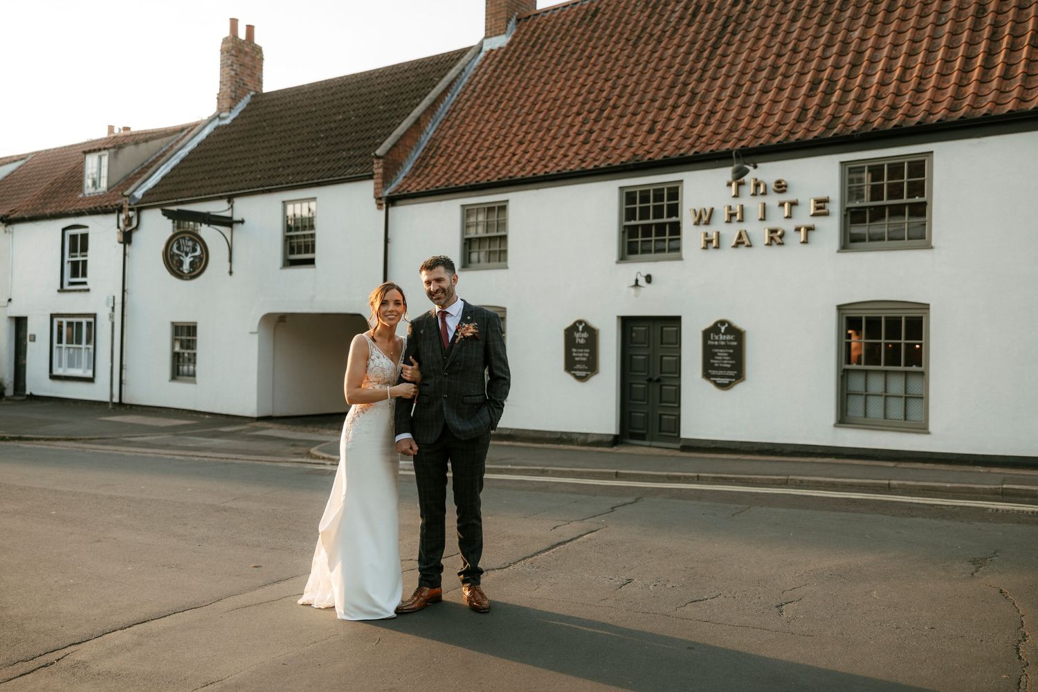 A couple poses outside The White Hart, a traditional English pub with whitewashed walls.