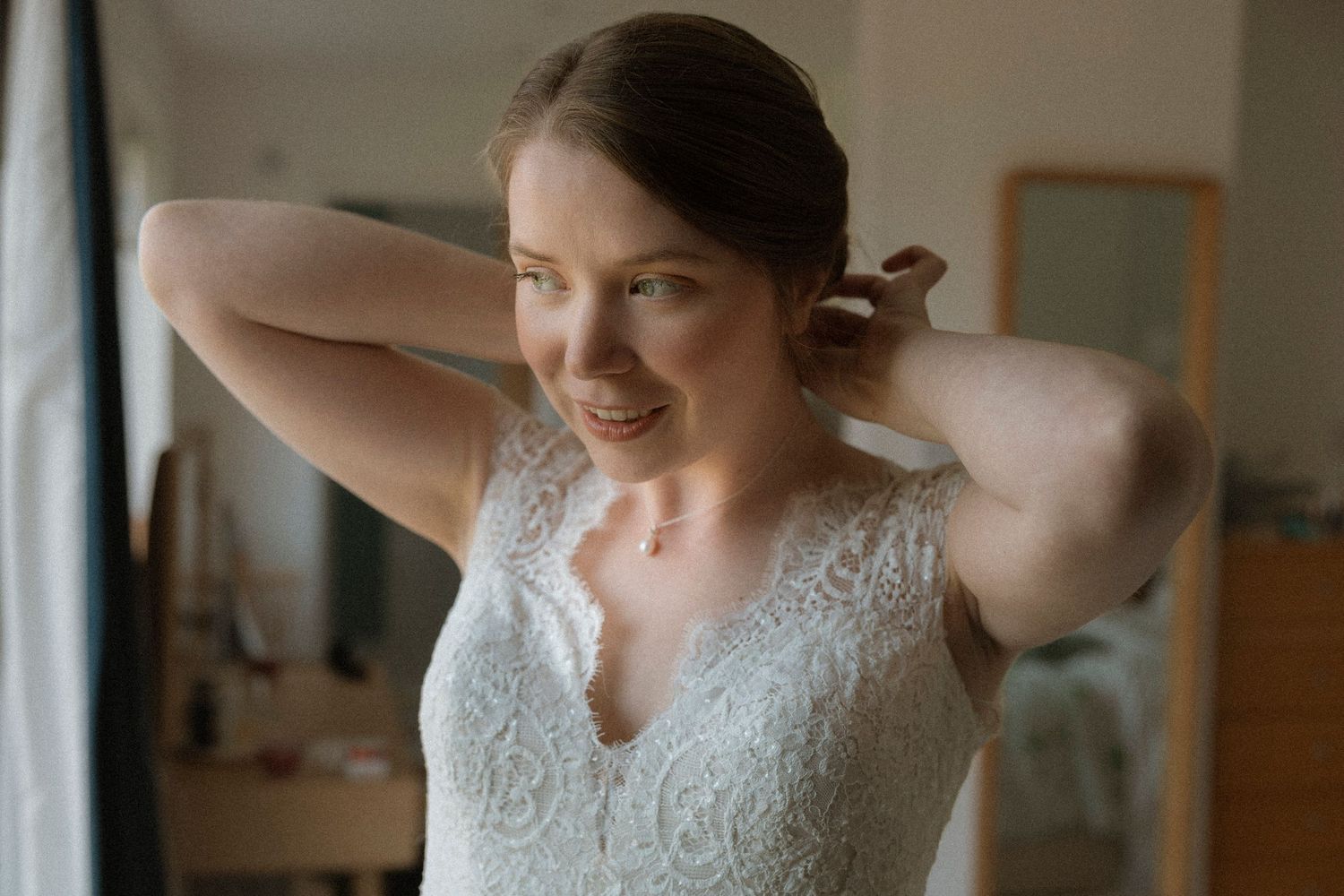 Bride in lace wedding dress adjusting her hair while smiling in a mirror reflection.