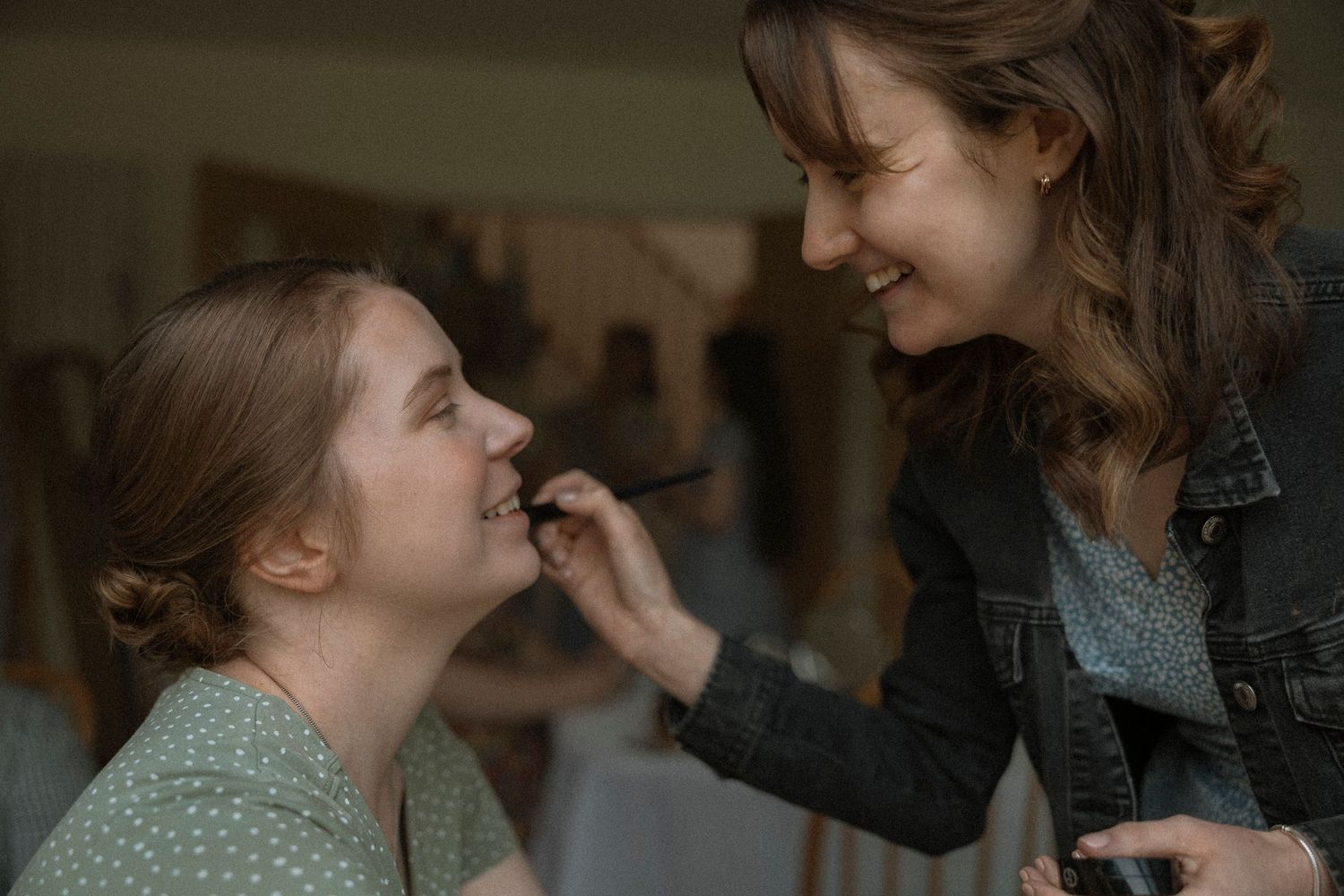 A makeup artist applying lipstick to a smiling woman in a bright studio setting.