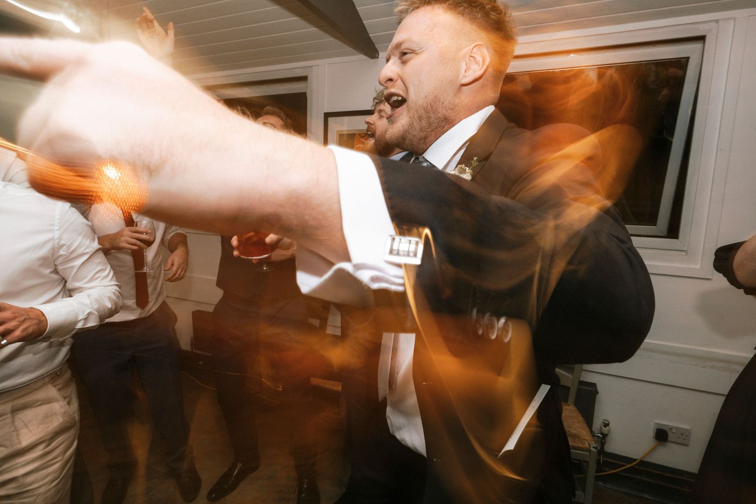 Man in suit dancing energetically at a wedding reception party with warm lighting effects.