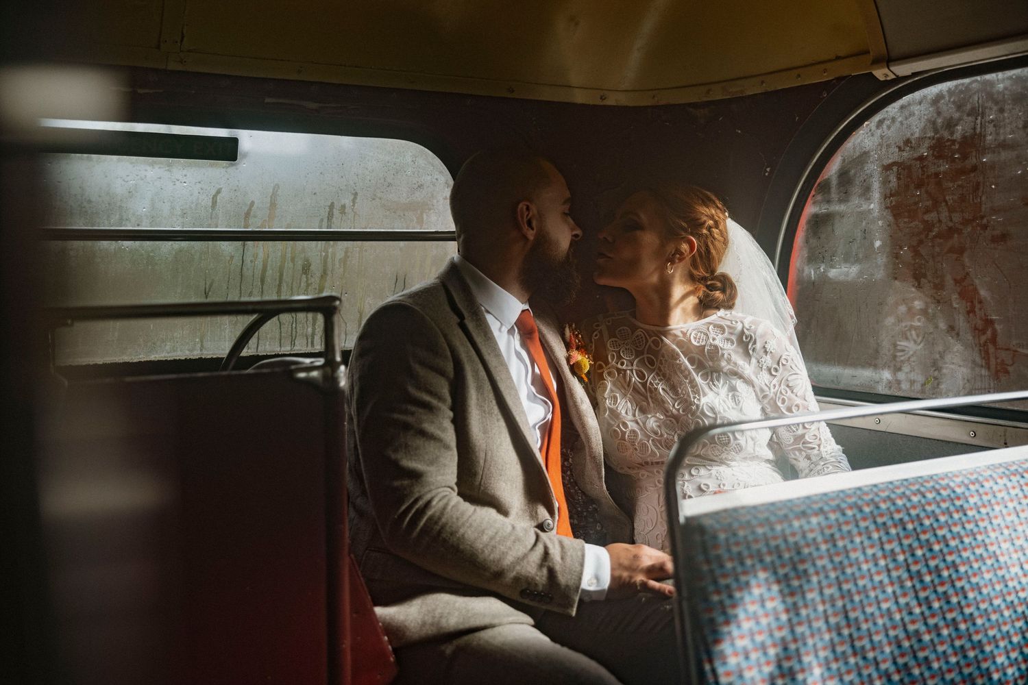 A bride and groom share a romantic kiss inside a vintage bus, with warm light highlighting their wedding attire.