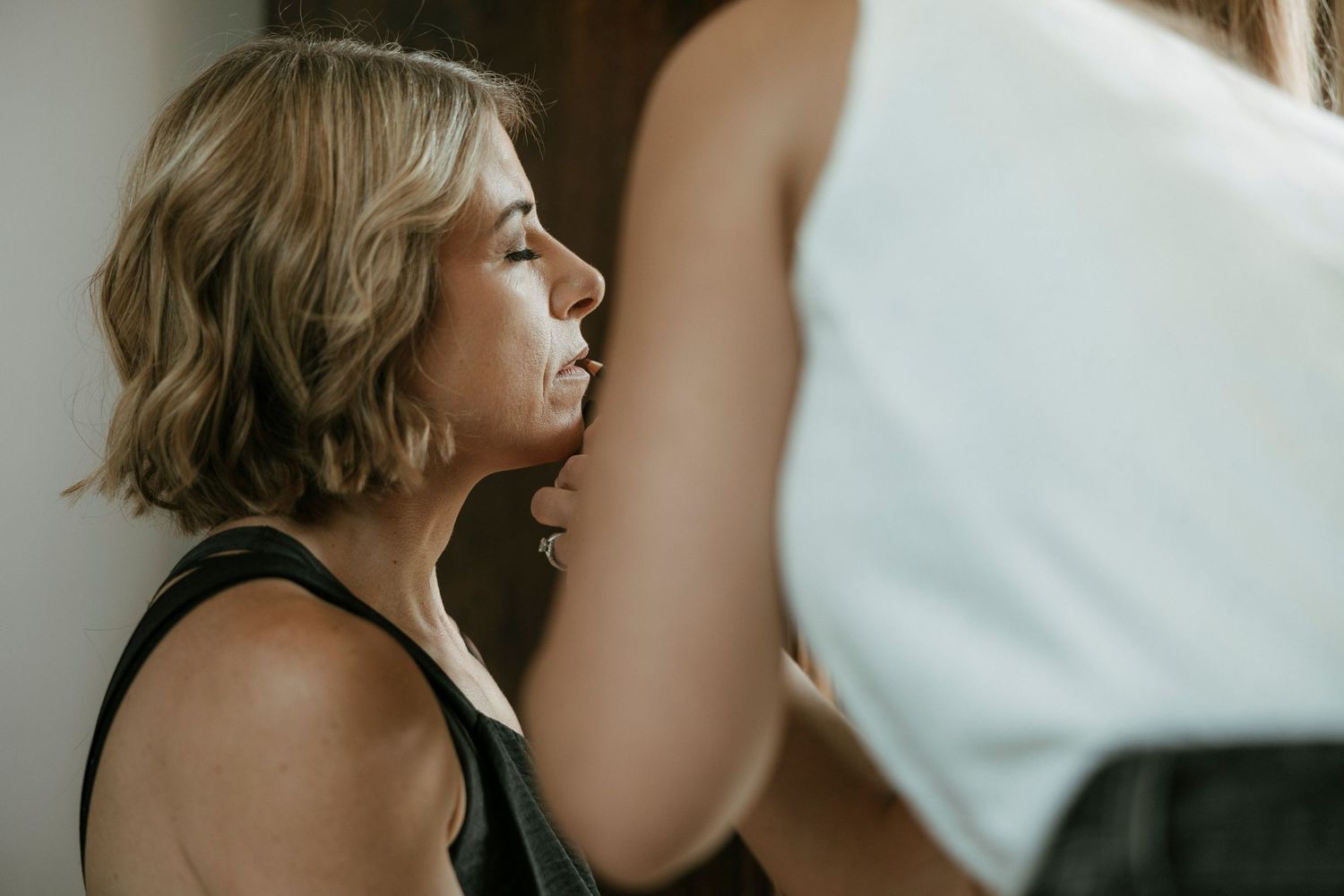 A woman with short blonde hair in a black tank top receives a beauty treatment from a professional stylist.