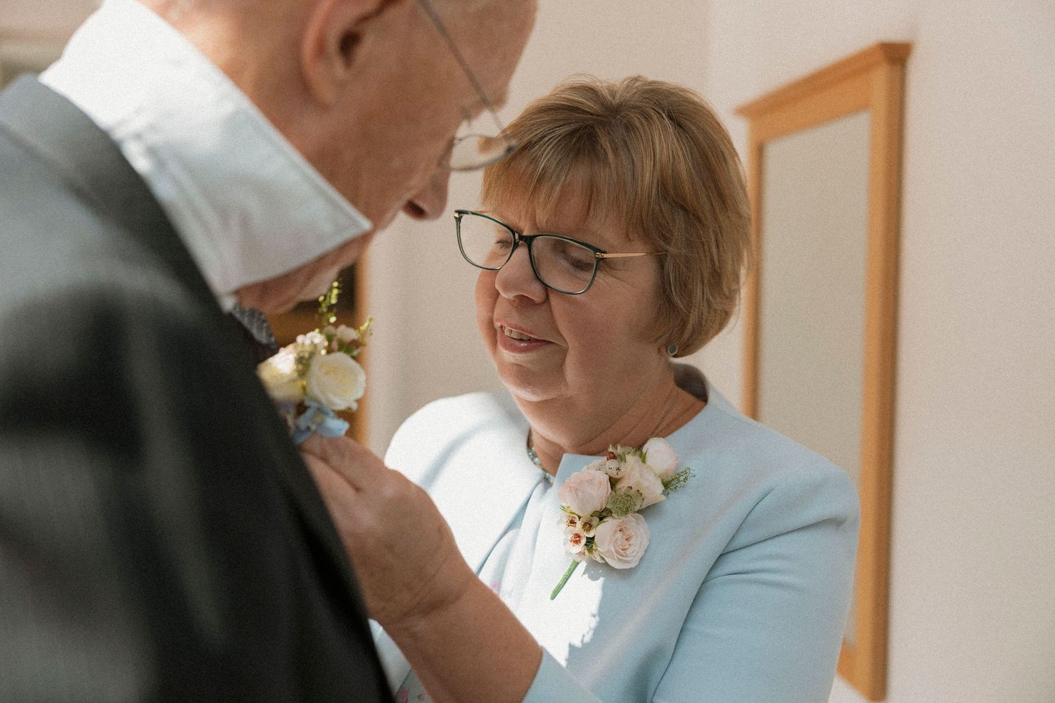Woman in blue dress pinning boutonniere on man in suit at wedding ceremony.