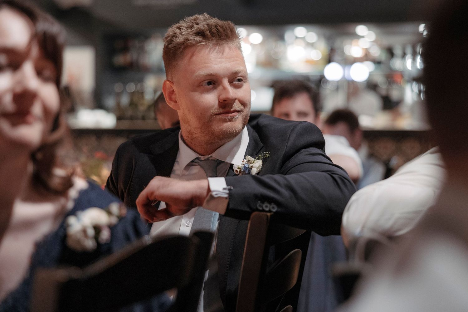 A well-dressed man in a suit checks his watch at an elegant indoor event or wedding reception.