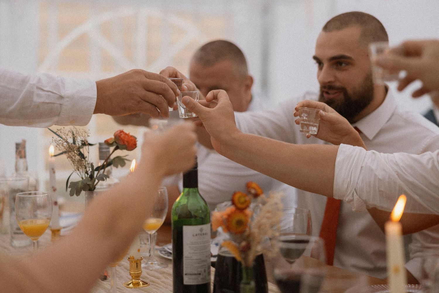 Guests clinking shot glasses in a toast at an elegant wedding reception dinner table with candles and wine.