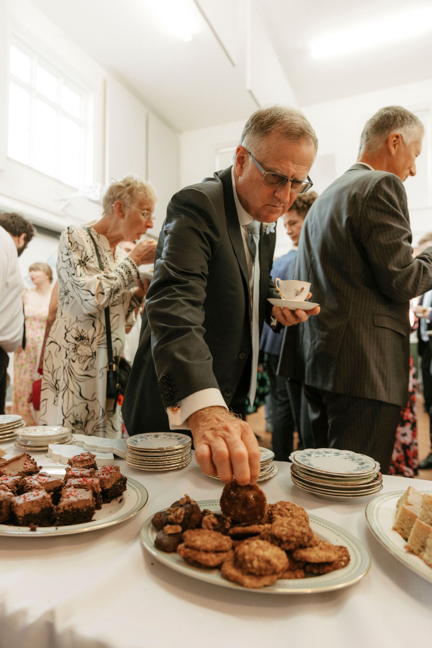 Man in dark suit selecting cookies from a dessert table at a formal reception event.