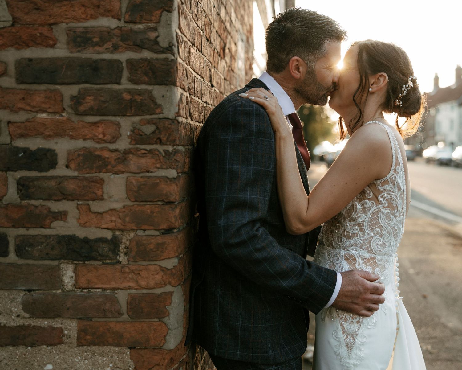 A romantic moment between newlyweds against a rustic brick wall at sunset.
