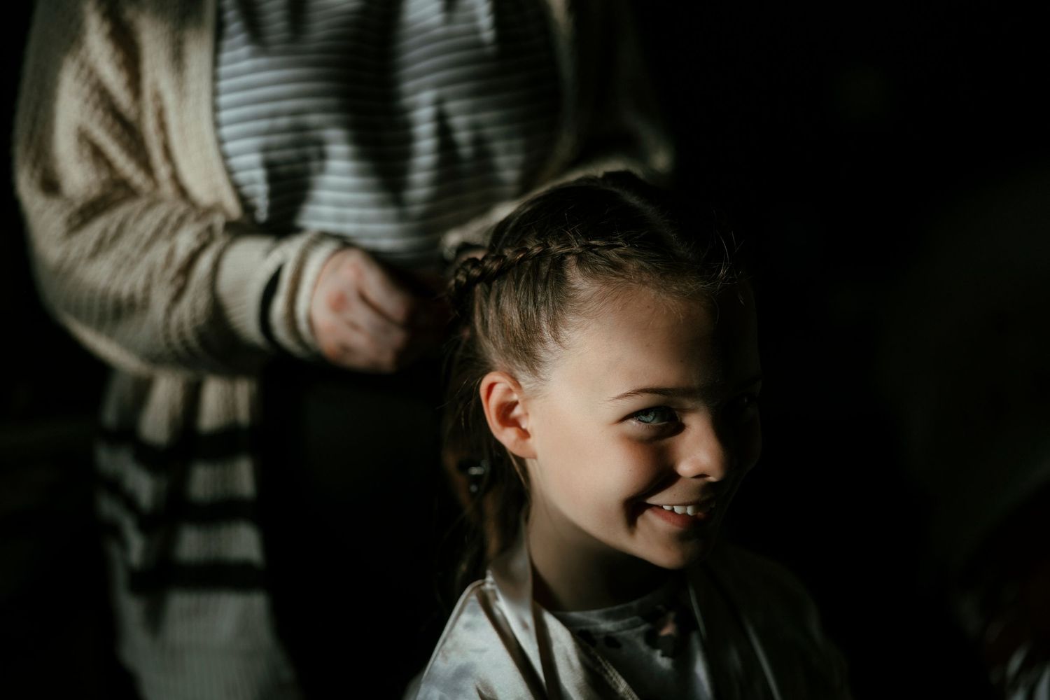 A young customer smiles while getting a haircut at a barbershop in moody lighting.