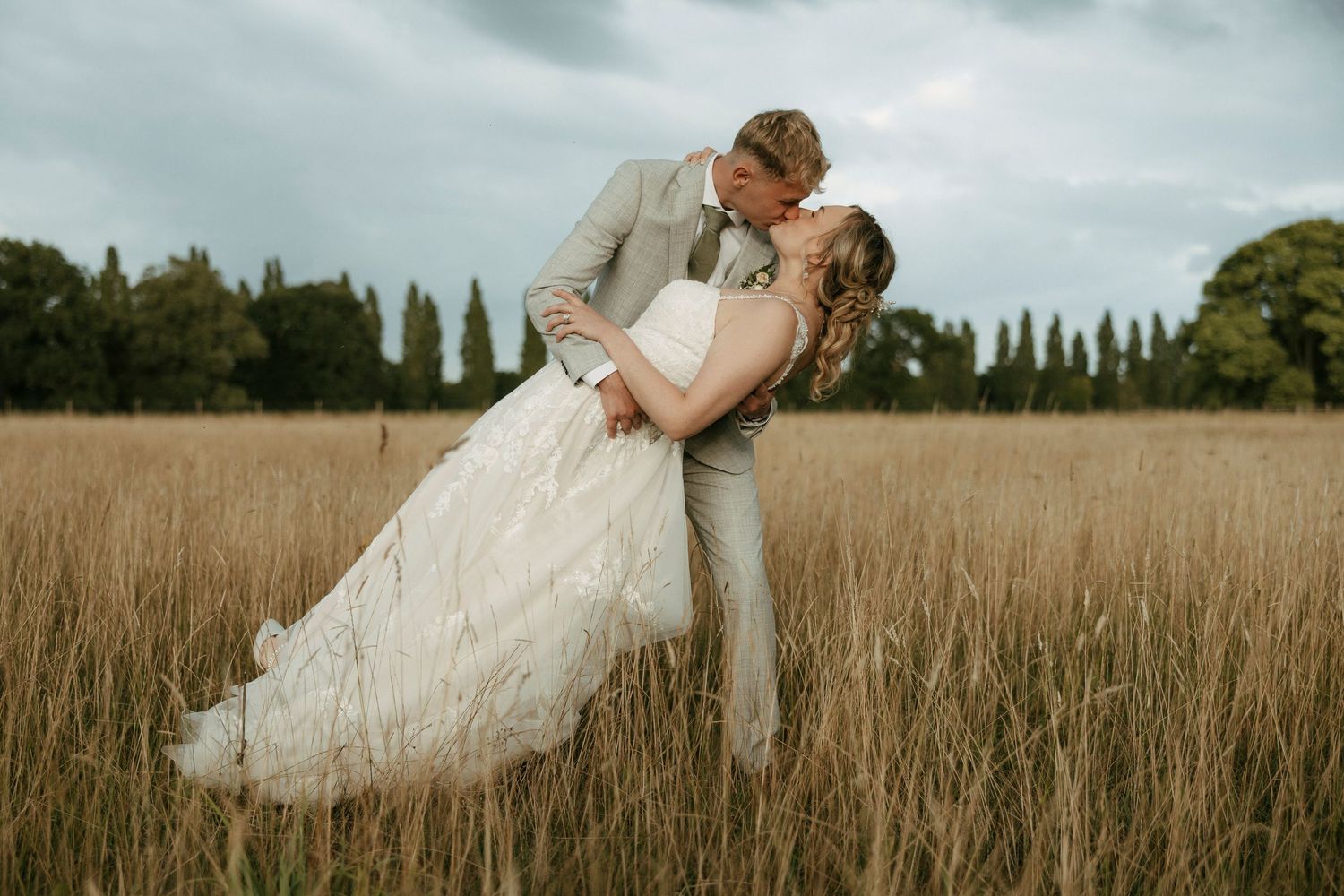 A couple in wedding attire embraces in a golden wheat field during sunset.