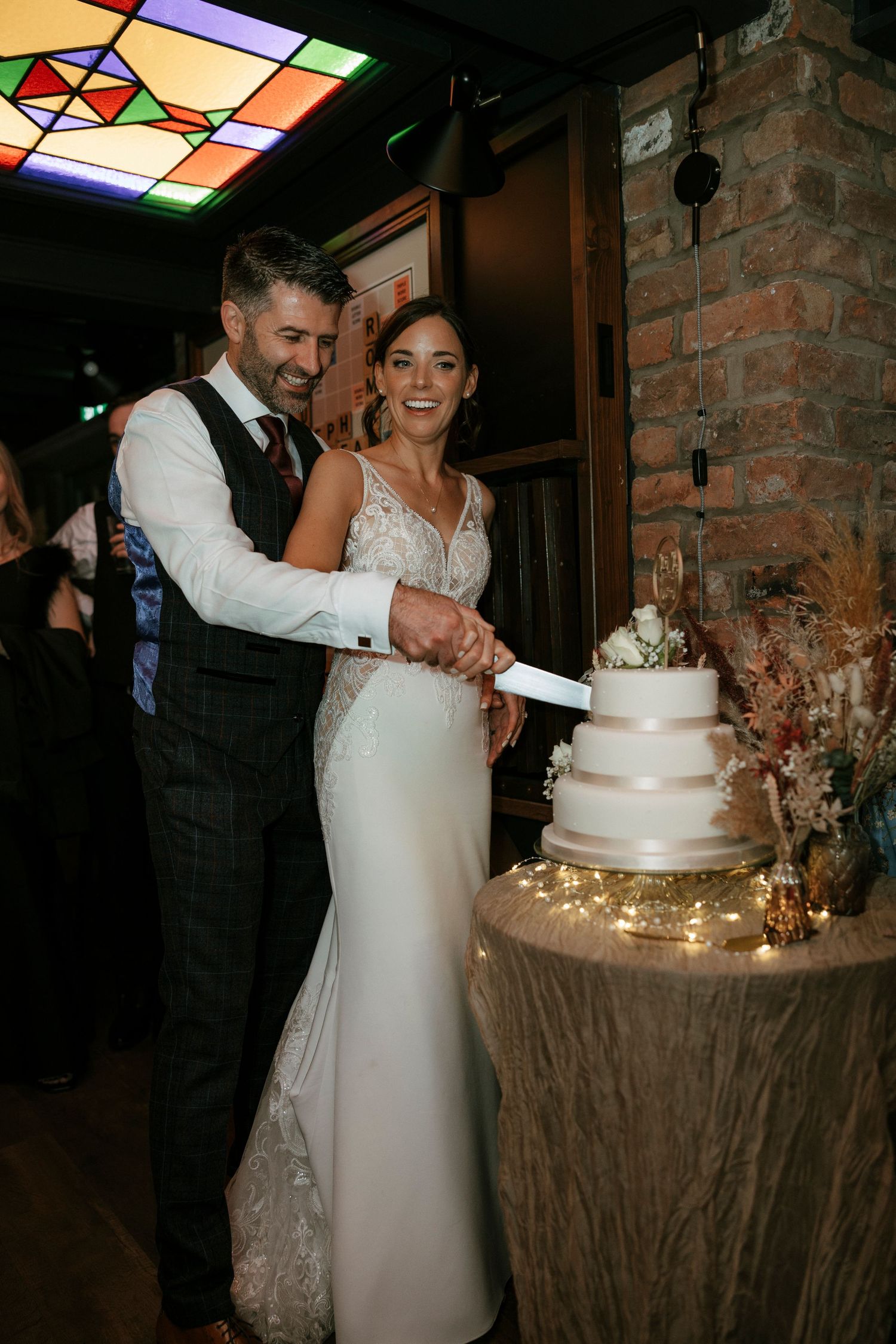 Bride and groom smiling while cutting their white three-tier wedding cake at their indoor wedding reception.