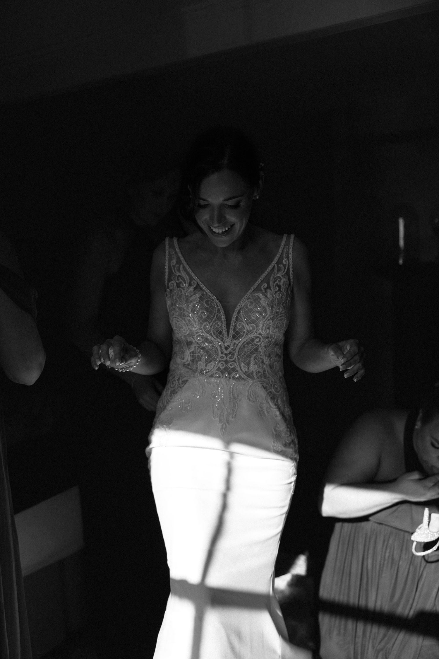 A joyful figure dances in a black and white photo wearing a lace-detailed top and white pants with dramatic lighting.