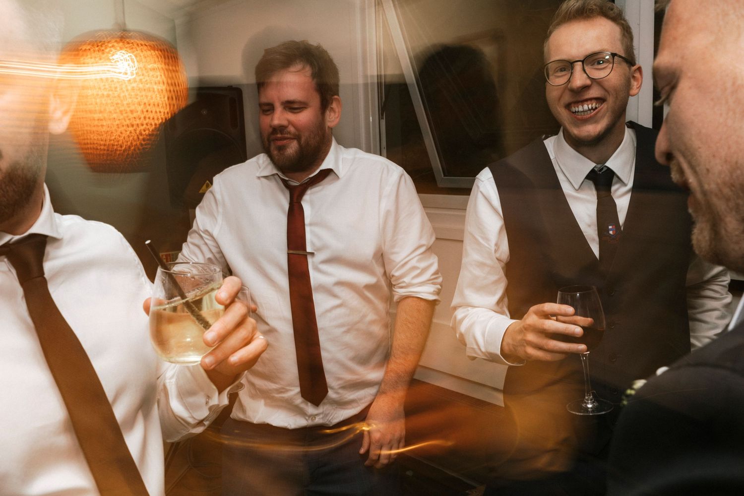 Men in dress shirts and ties laughing and drinking wine at a formal celebration event.