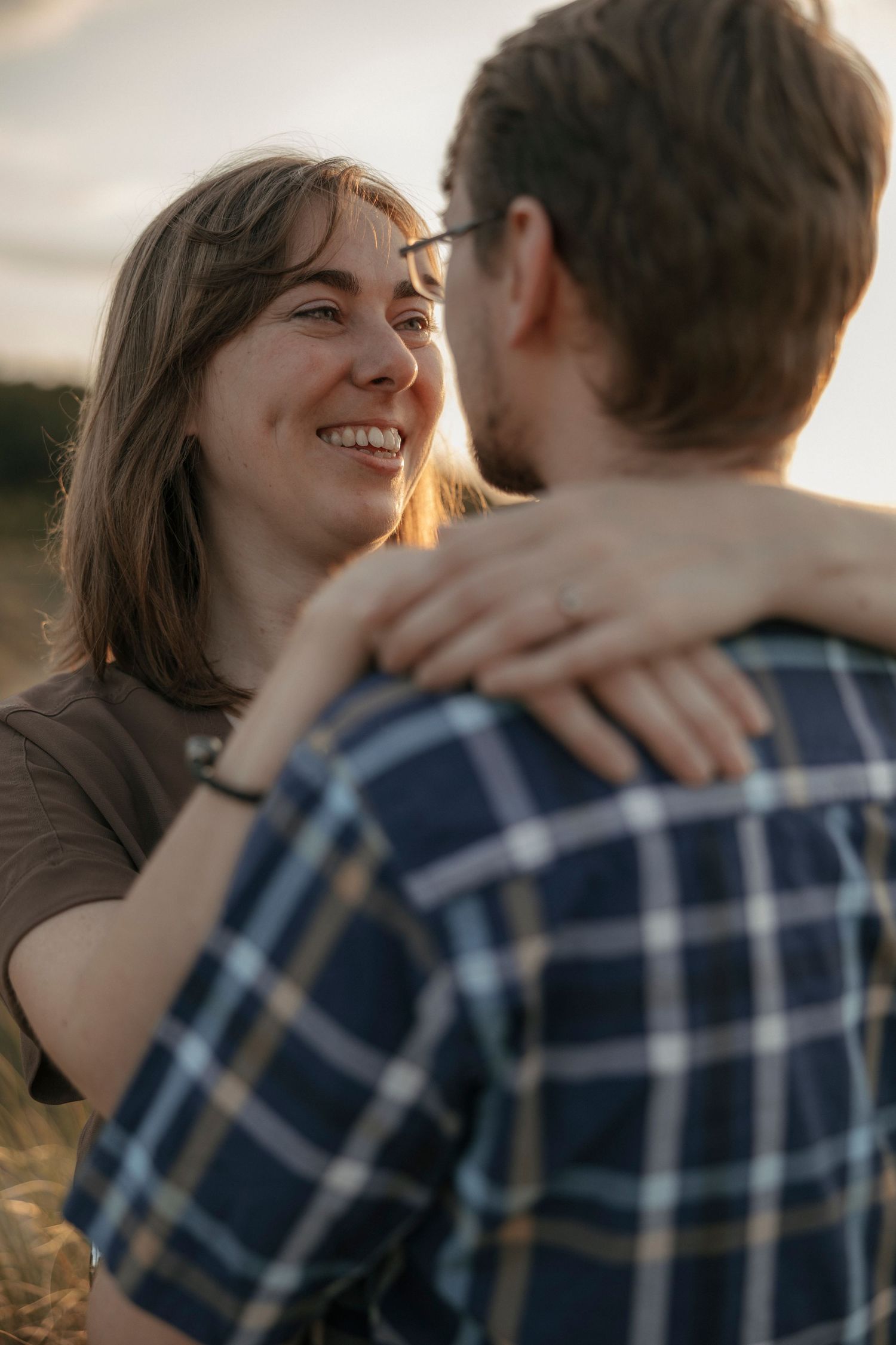 Woman smiling warmly while embracing her partner outdoors during golden hour.
