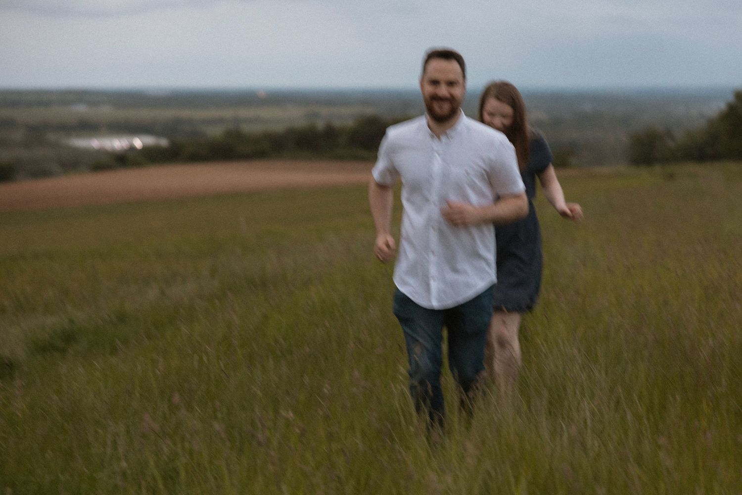 Couple running playfully through tall grass in blurred motion shot.