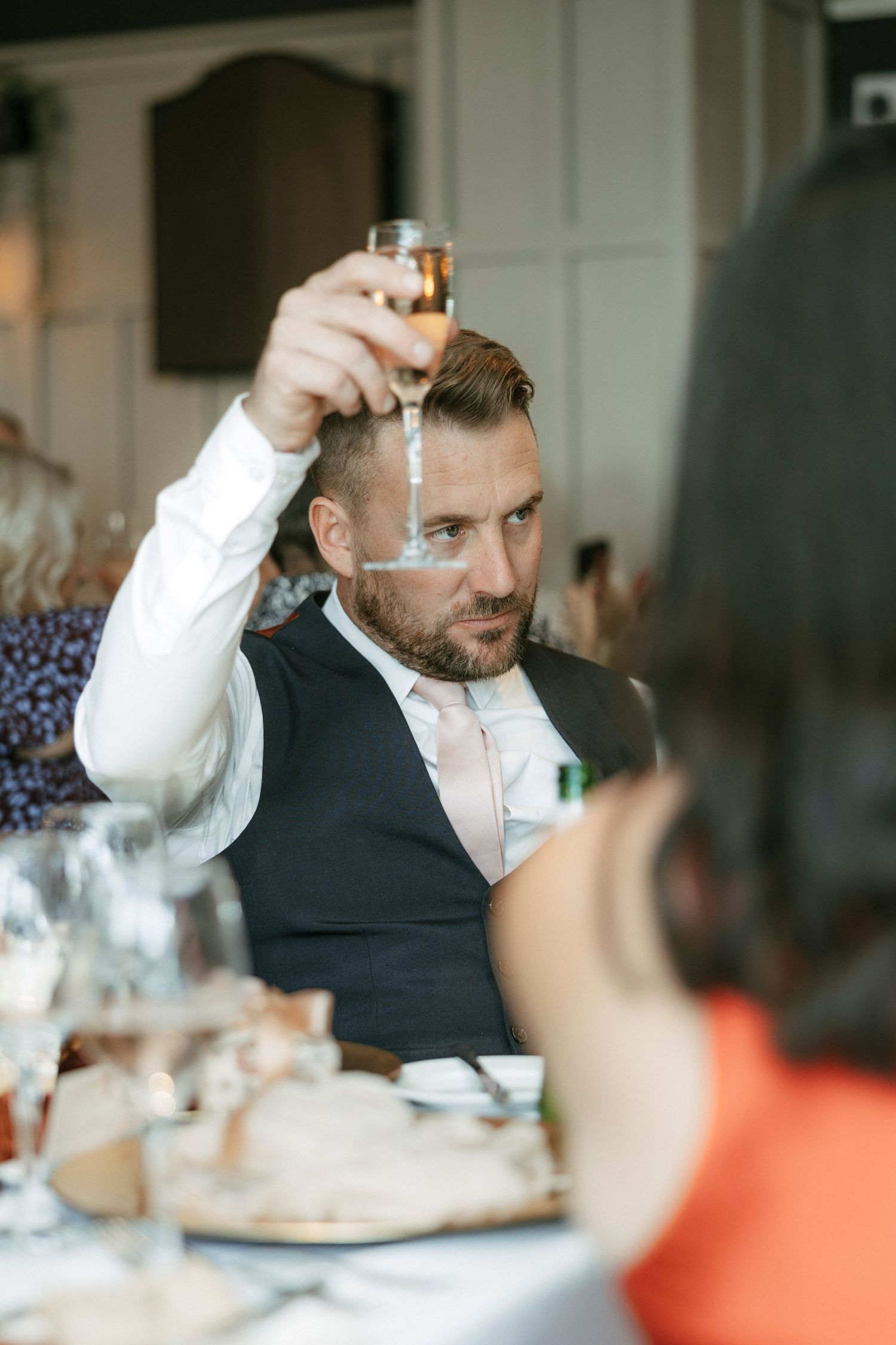 Bearded man in vest raising champagne glass at formal dinner table during celebration event.