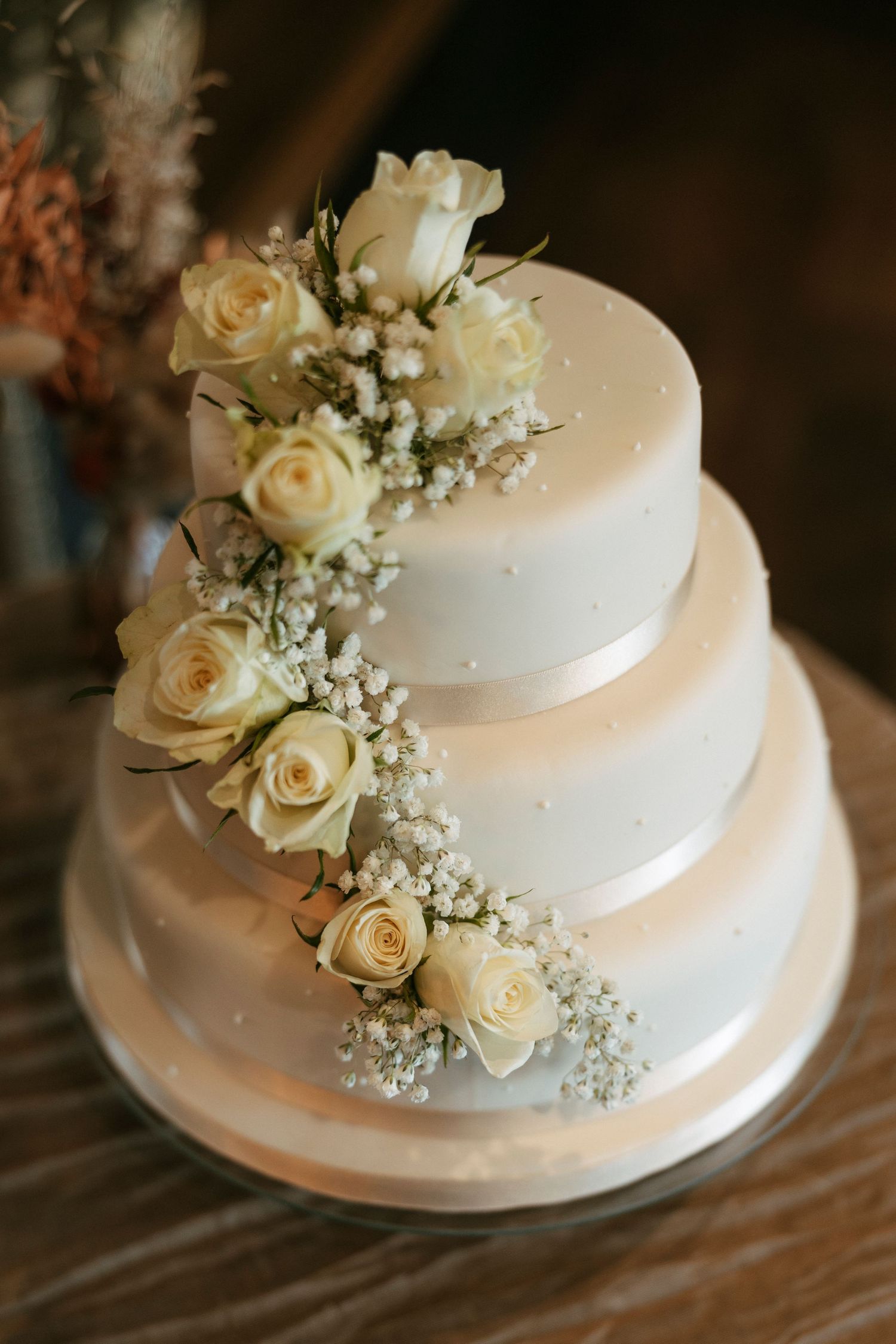 White three-tier wedding cake decorated with cream roses and baby's breath in cascading design.