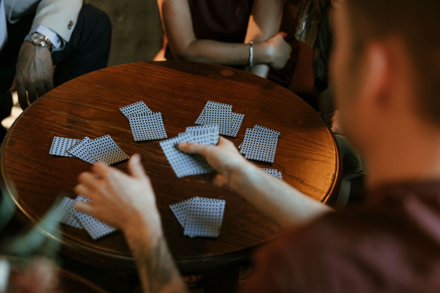 Playing cards scattered on a round wooden table during a casual card game.