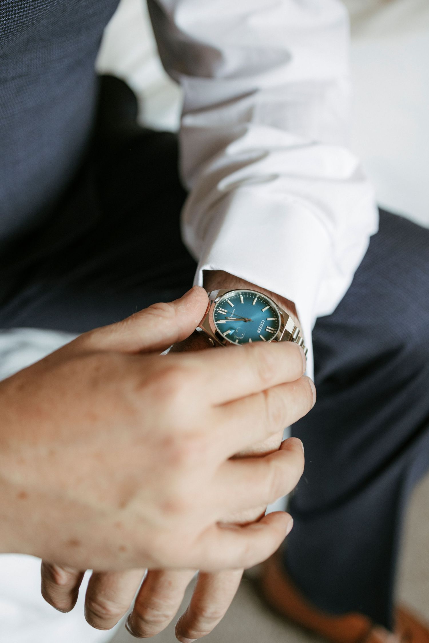 Groom adjusting elegant silver watch with blue dial on wedding day.