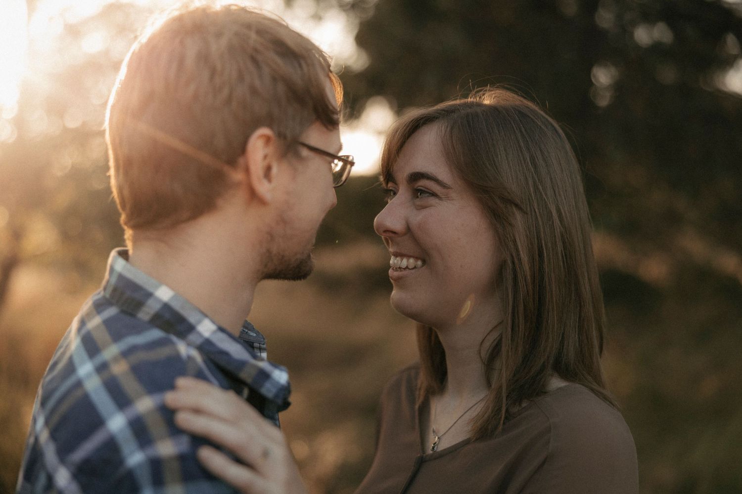 Couple sharing a romantic moment smiling at each other in warm golden sunset light outdoors.