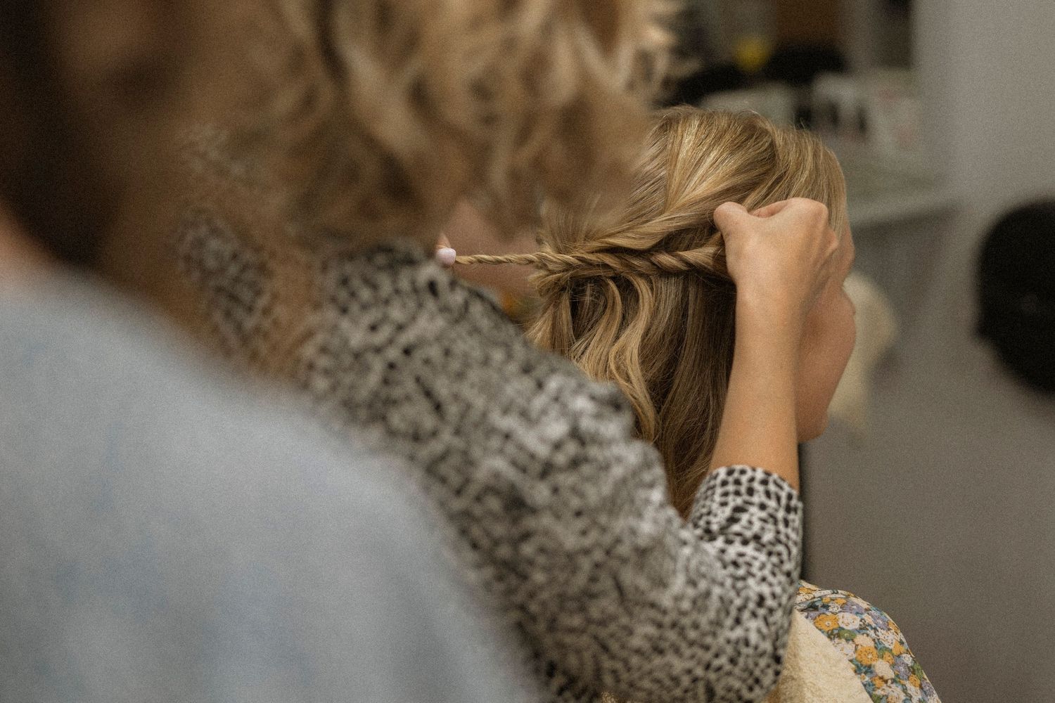 Hairstylist braiding a client's blonde hair in a salon setting.