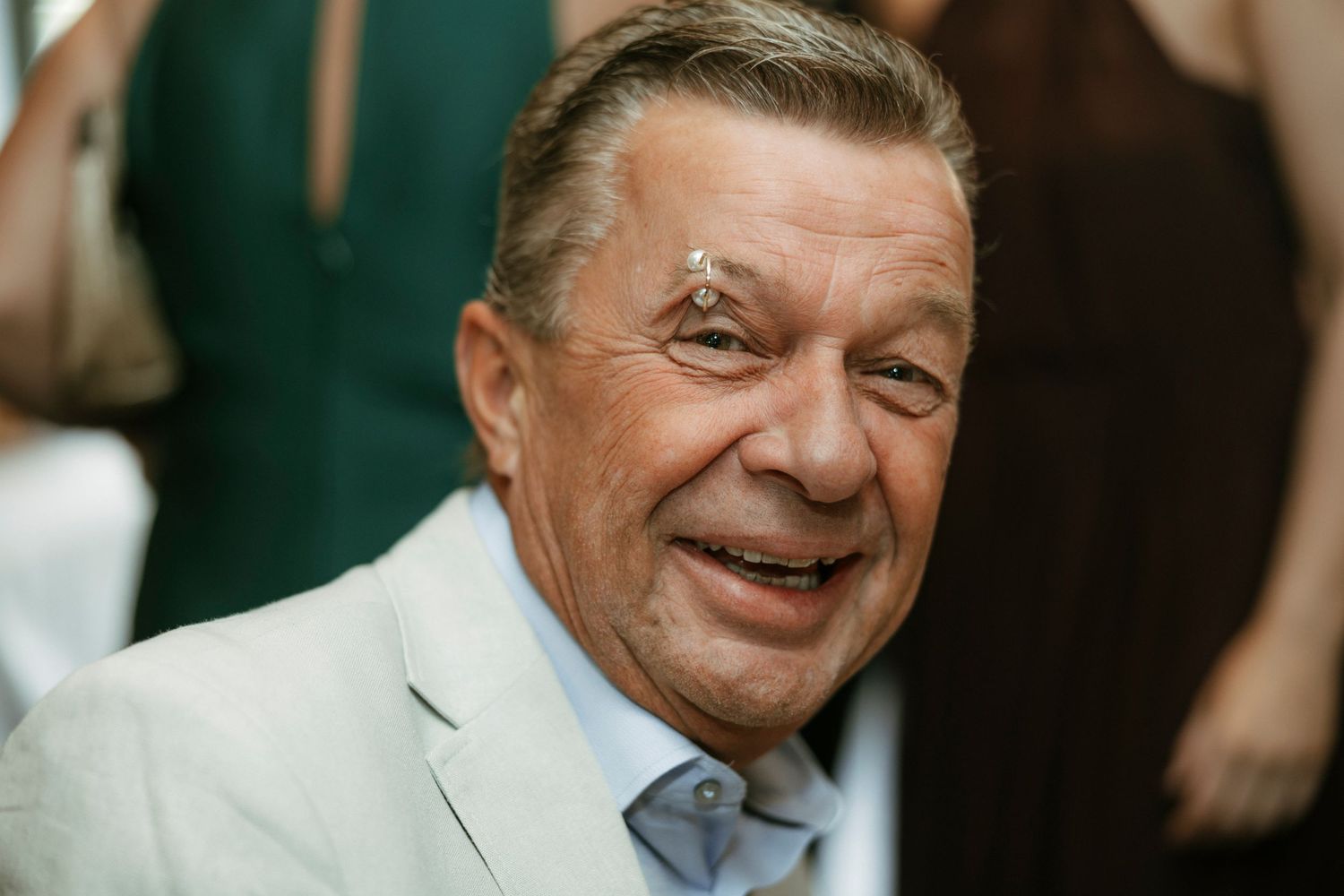 A gentleman in formal white jacket smiling warmly at a social event.