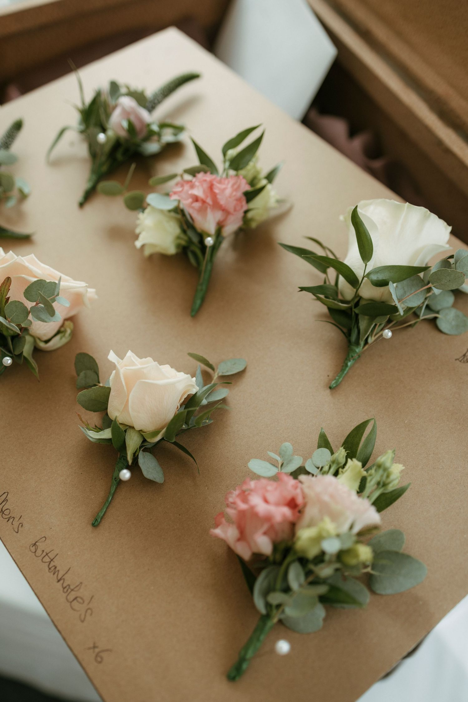Elegant wedding boutonnieres with white roses and pink carnations on kraft paper box.