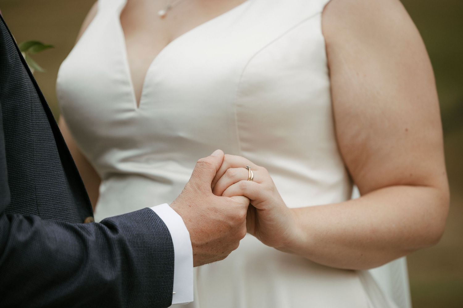 Bride and groom holding hands during wedding ceremony, showcasing wedding ring in close-up shot.