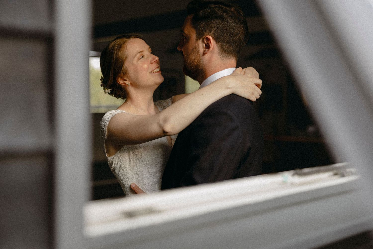 Bride and groom share a romantic dance viewed through a window frame on their wedding day.