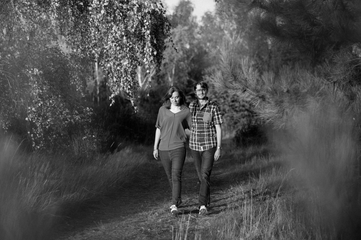 Black and white photo of a couple walking together on a nature path lined with tall grass.