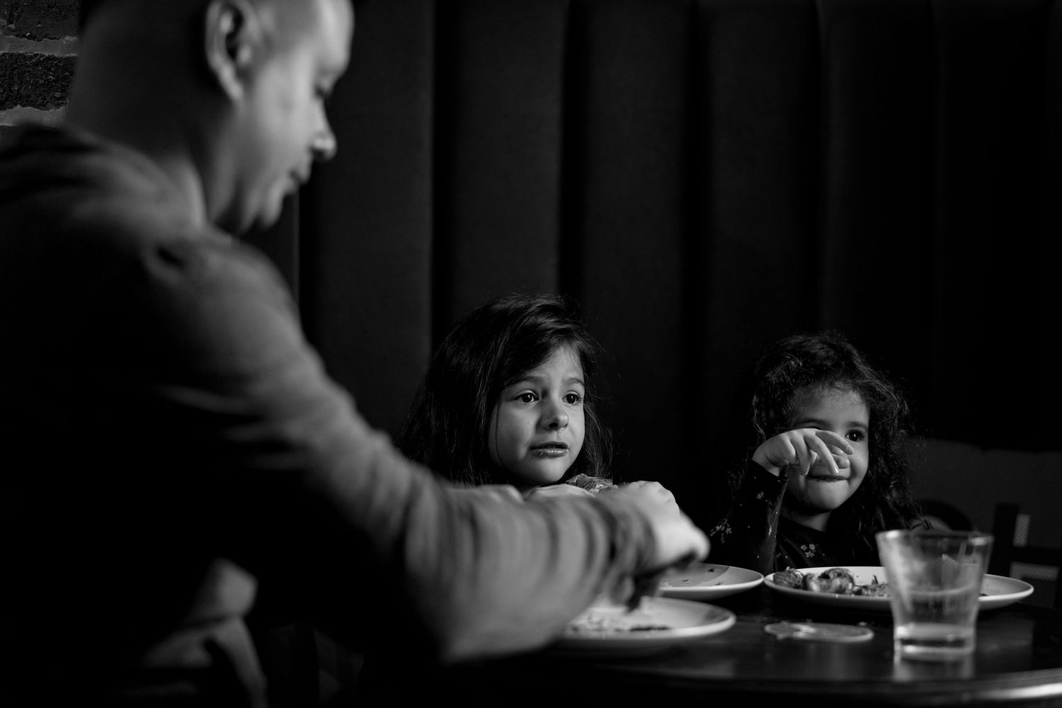 Black and white photo of a man dining with two young girls at a restaurant table with plates and glasses.