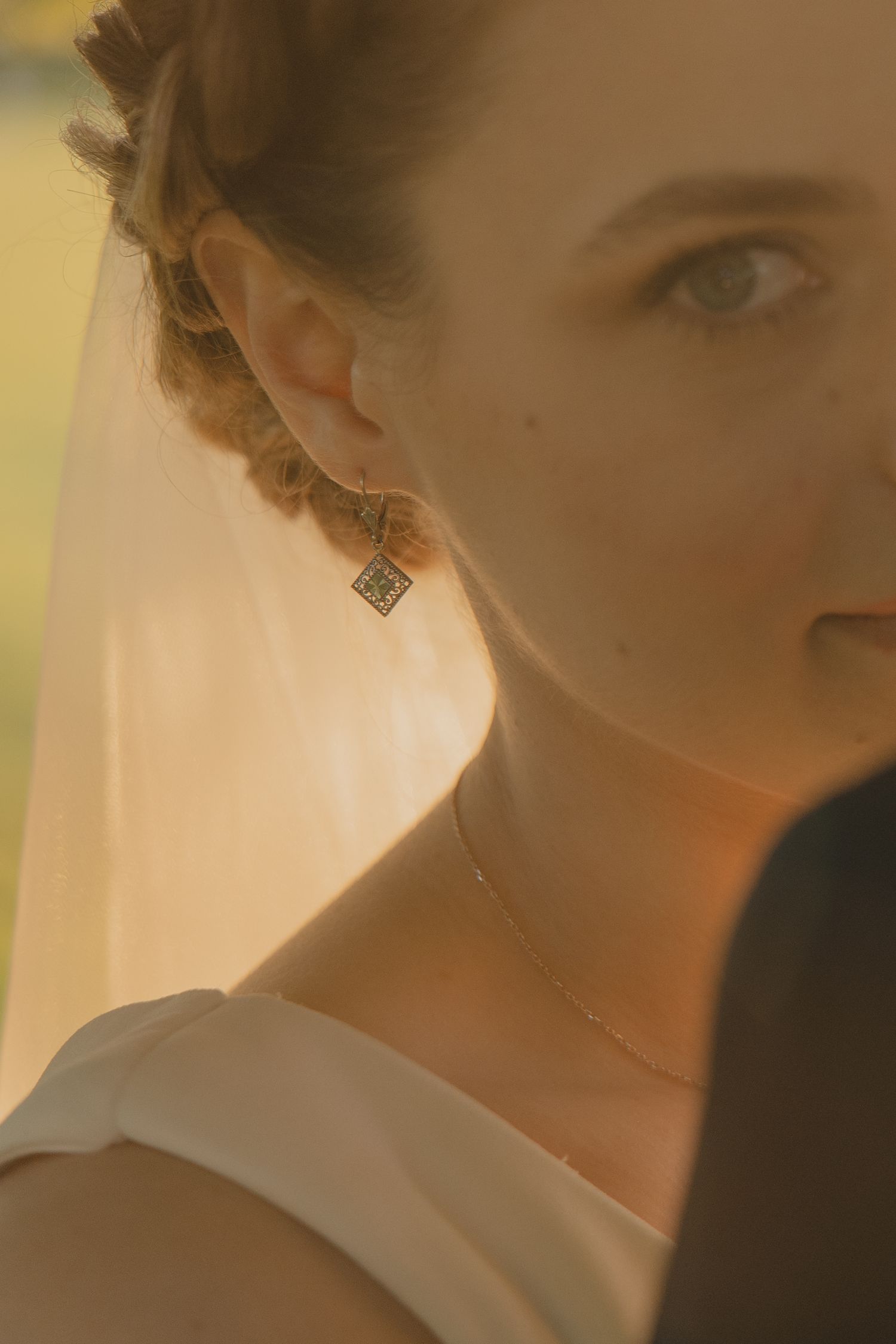 Close-up of a bride wearing a diamond earring and delicate necklace, with a veil in warm golden light.