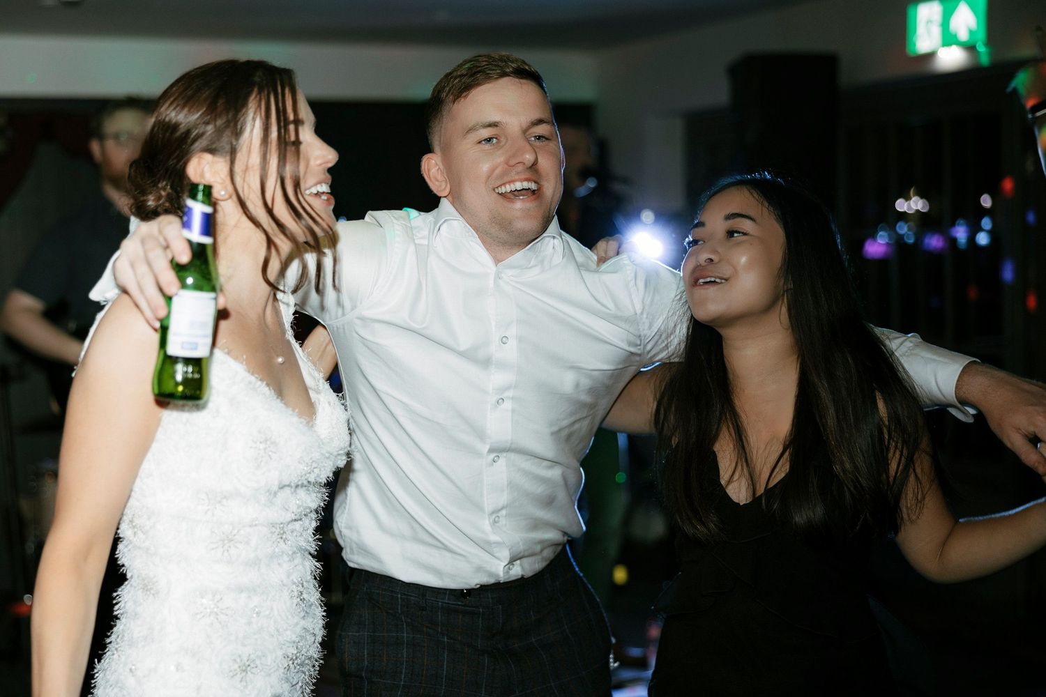 People dancing and celebrating at a lively party with bottles and colorful lights visible in the background.